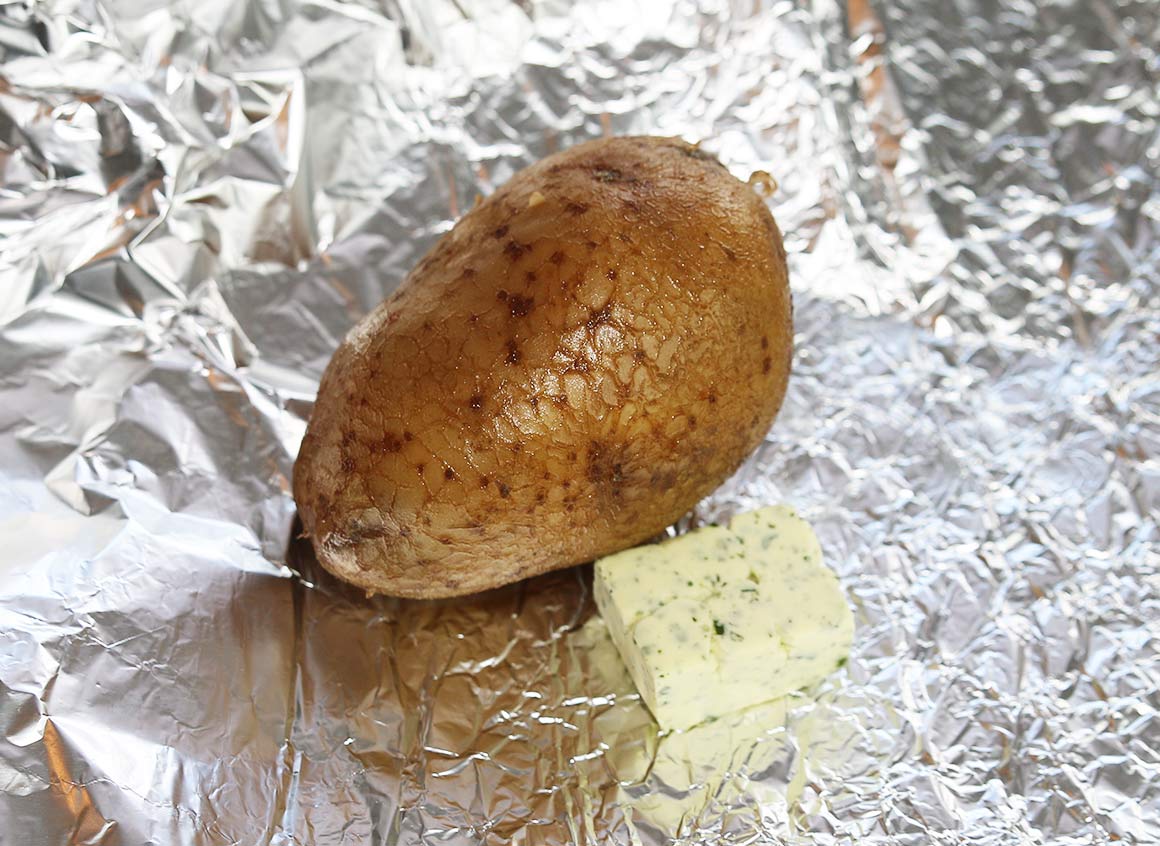 Kartoffeln auf ein Stück Alufolie geben, Kräuterbutter hinzufügen.